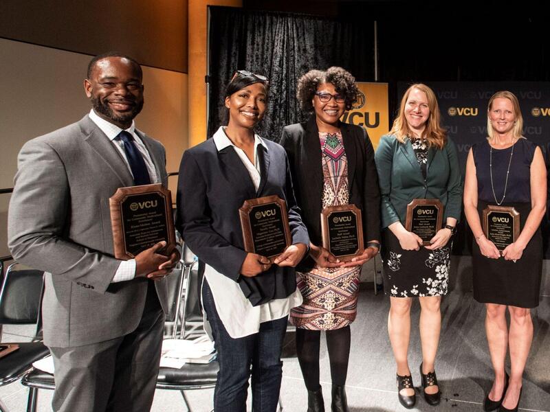 Five award winners lined up holding their plaques with two others joining them.