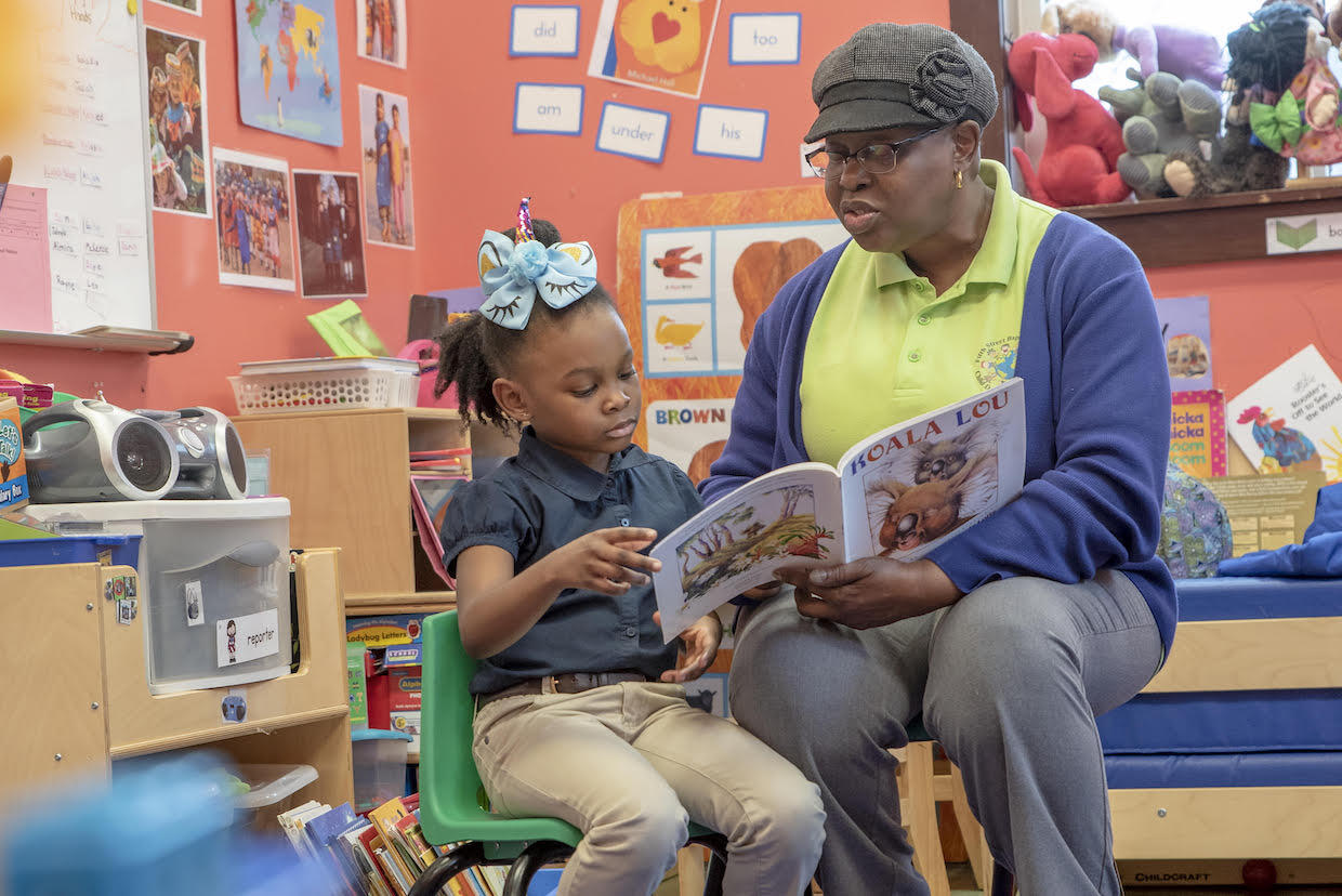 A woman and her daughter are seated in a classroom reading a book.