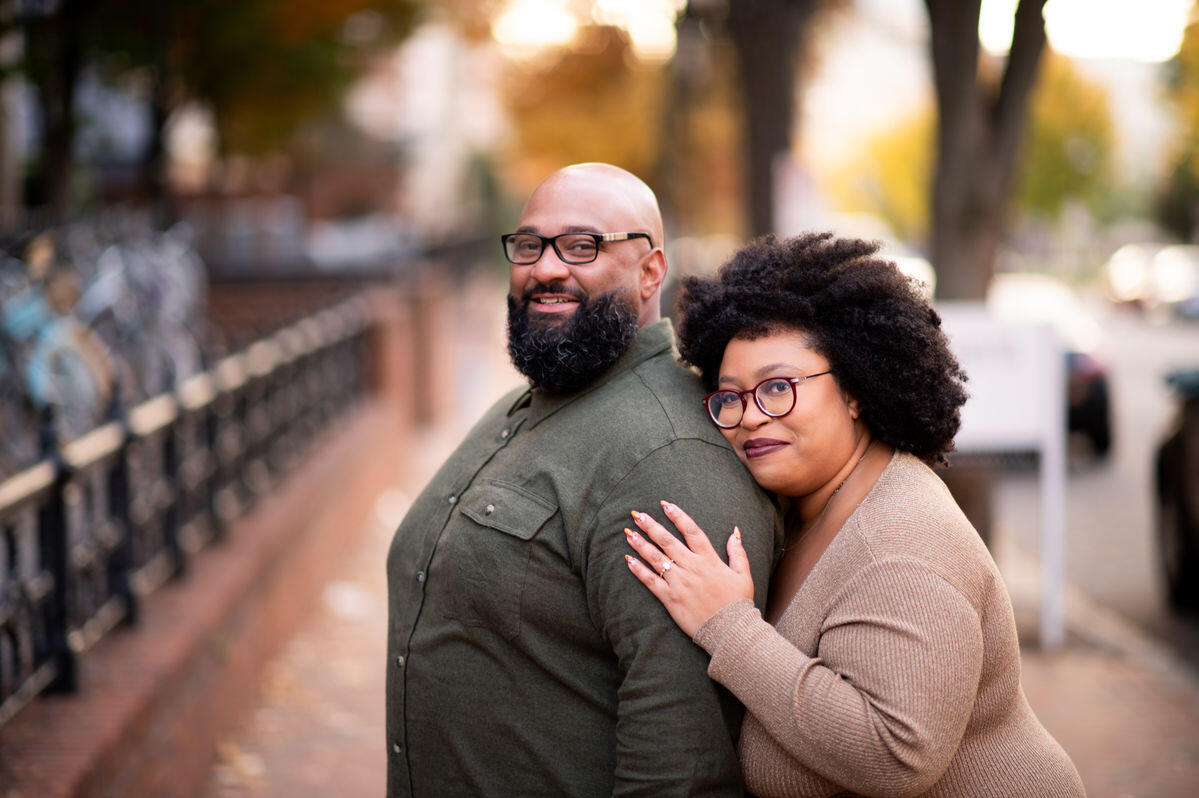 A photo of a man standing and a woman holding him from behind. 