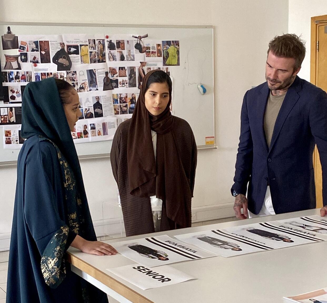 Two women and one man standing at a table with photos on it 
