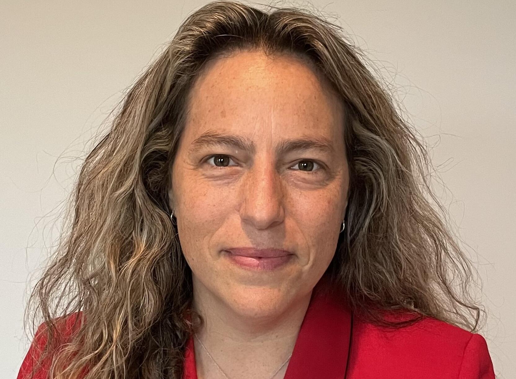 A photo of a woman wearing a red suit jacket from the shoulders up. 