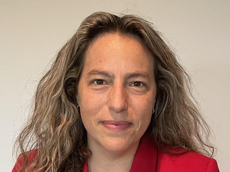 A photo of a woman wearing a red suit jacket from the shoulders up. 