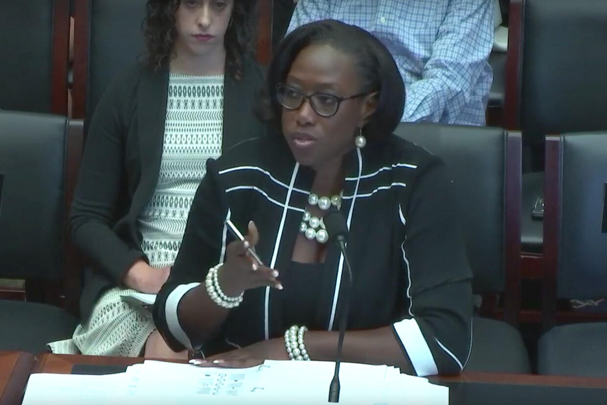 Woman seated at a table, speaking into a microphone.