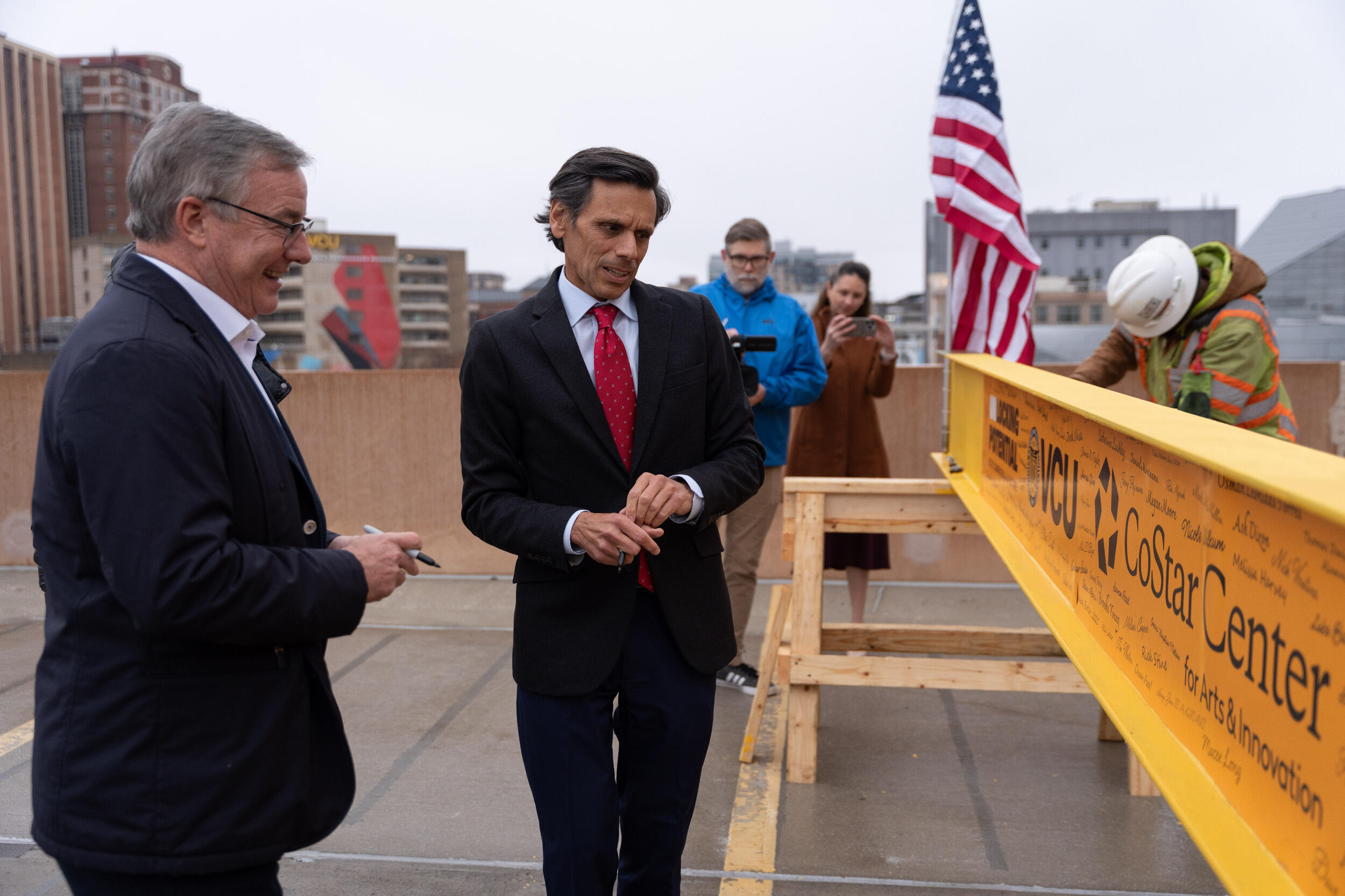 A photo of two men standing next to a yellow construction beam. 