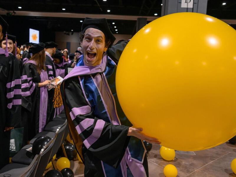 A man in a cap and gown holds a large yellow balloon.