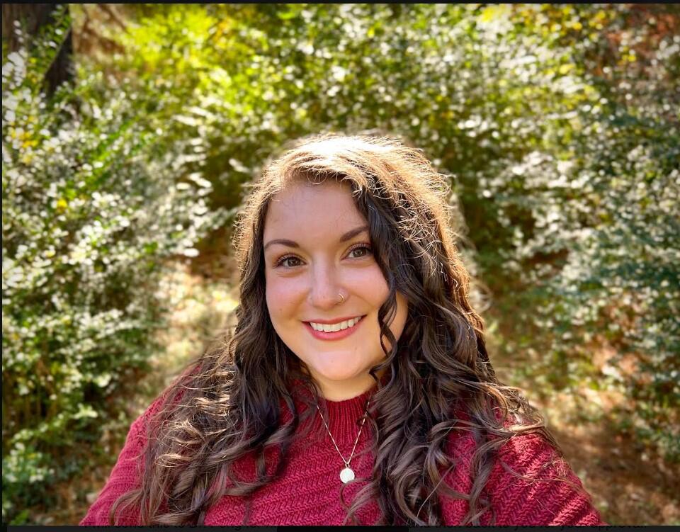 A photo of a woman standing in front of bushes. 