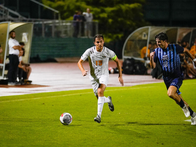 A photo of two men running on a soccer field towards a soccer ball. 