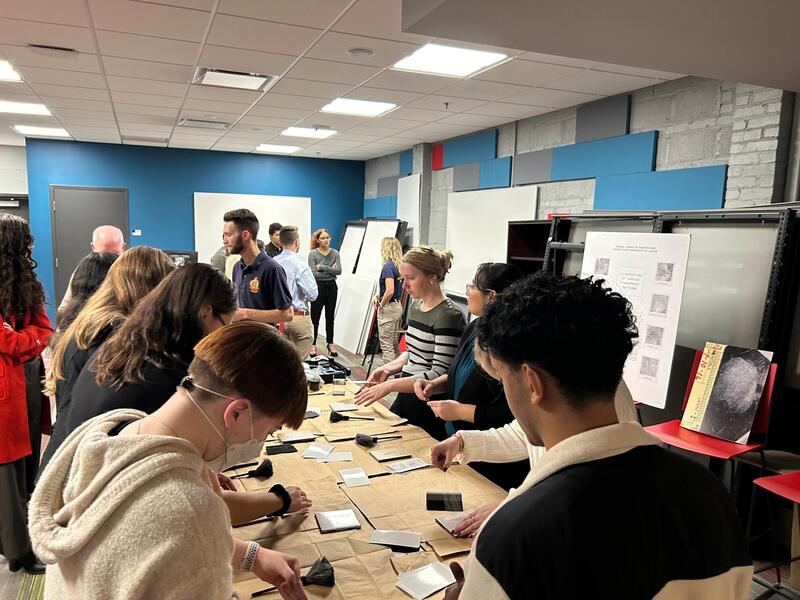 Seven people sitting at a table with five people at the other end of the room standing up 