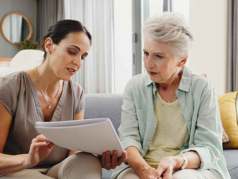 A woman holds a paper out to look at with an older woman.