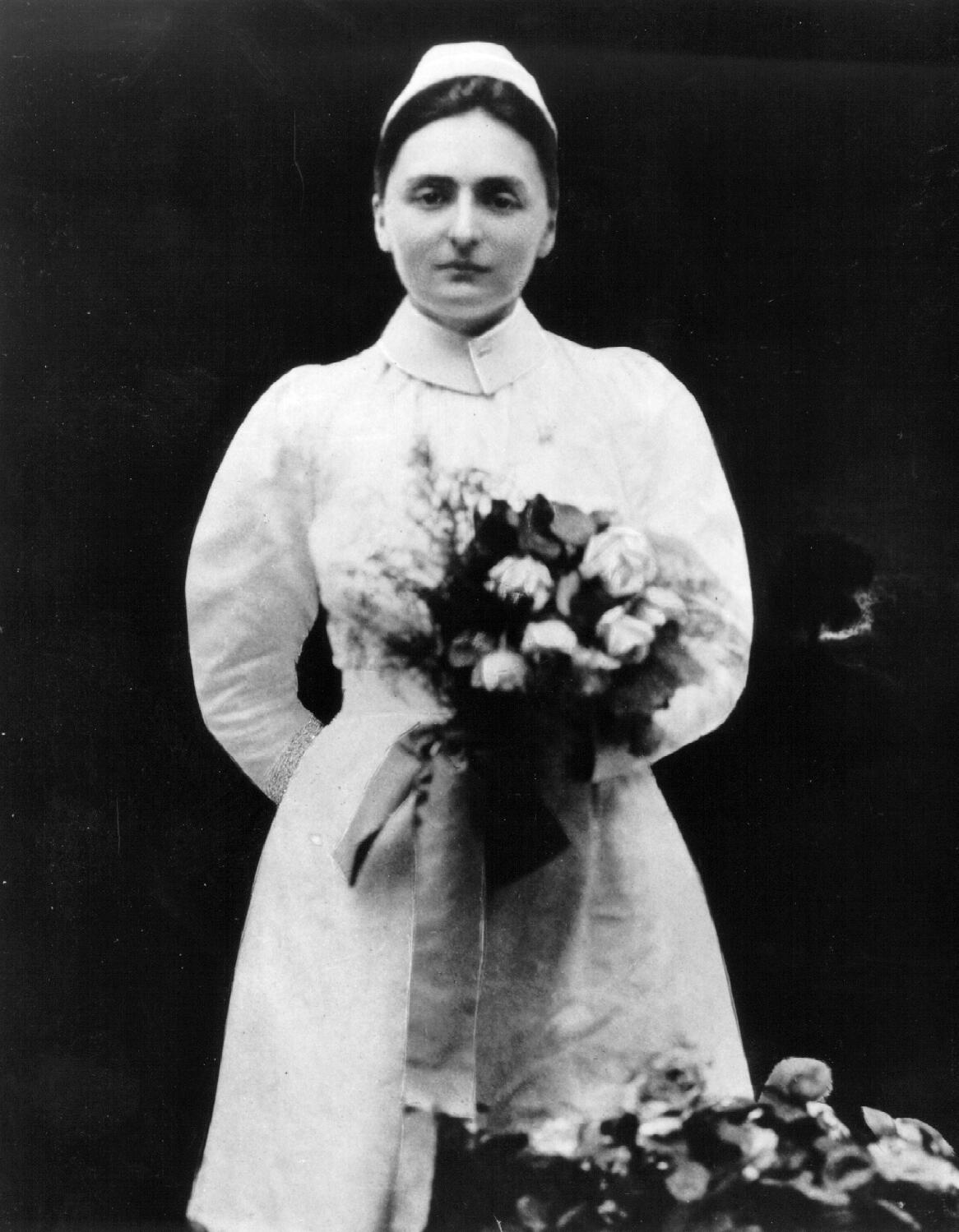 A black and white photo of a woman in a white nurse uniform holding a bouquet of flowers. 