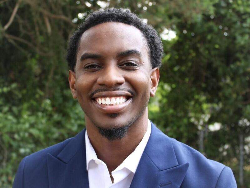 A photo of a man from the chest up. He is smiling and wearing a white button down shirt and a blue suit jacket. 