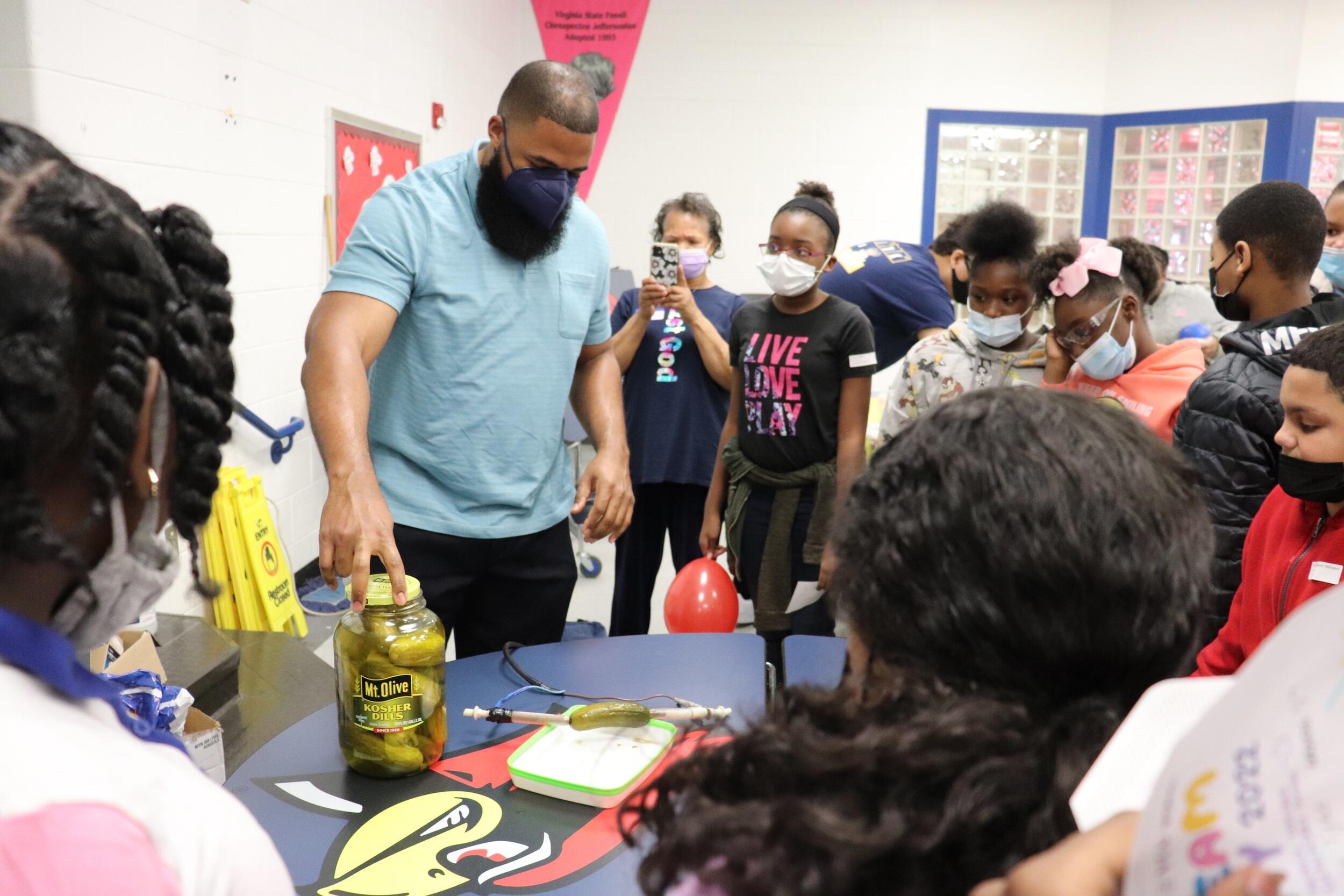 A professor showing a room full of students a pickle jar he is using as a battery