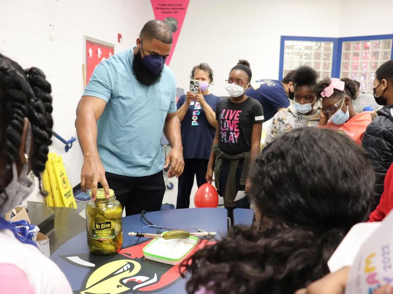 A professor showing a room full of students a pickle jar he is using as a battery