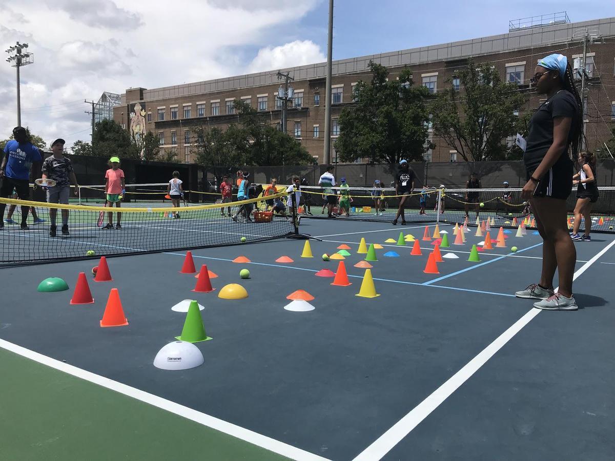 A tennis court covered in cones. Counselors and campers are standing around it. 