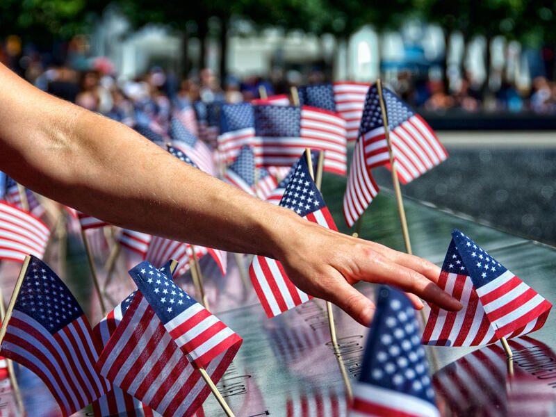 A photo of an arm outstretched with a hand touching a small American flag. There are many other small American flags around the arm and first flag. 