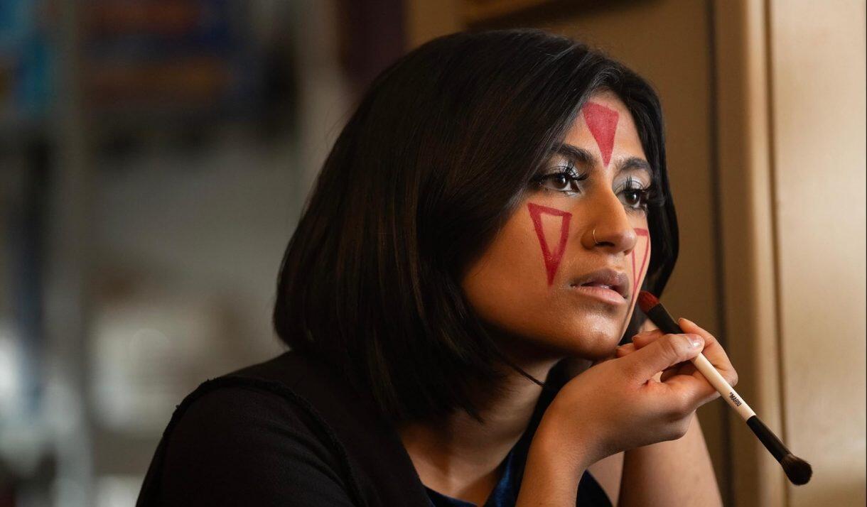 A photo of a woman painting red triangles on her face with makeup. 