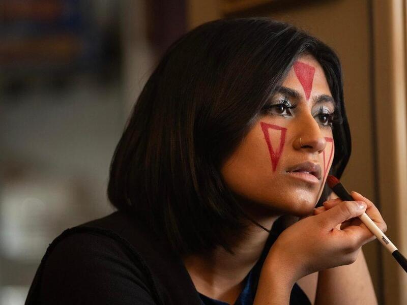 A photo of a woman painting red triangles on her face with makeup. 