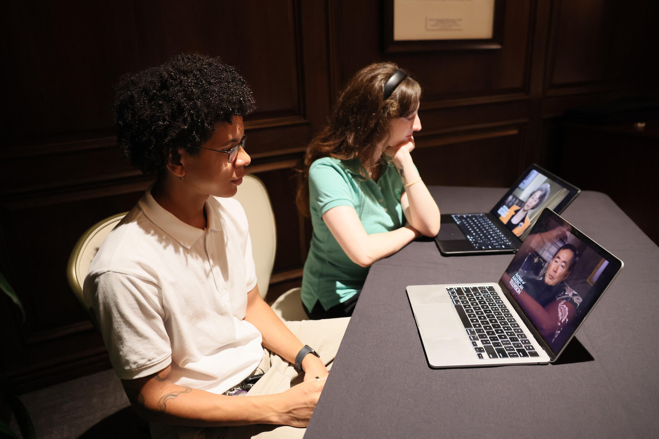 A photo of two students sitting at a table in front of two laptops. 