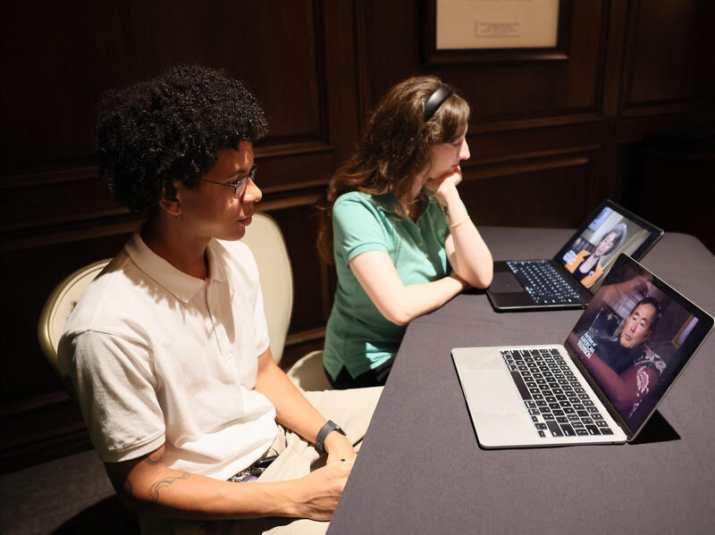 A photo of two students sitting at a table in front of two laptops. 