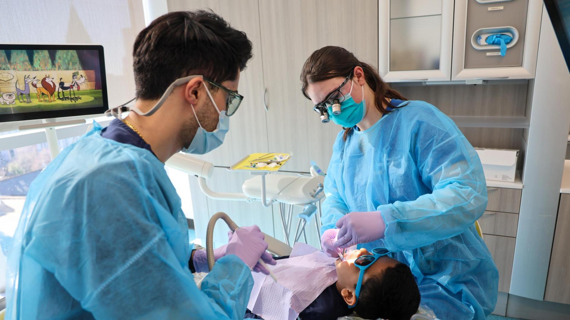 A photo of a man and woman doing a dental cleaning on a child. 