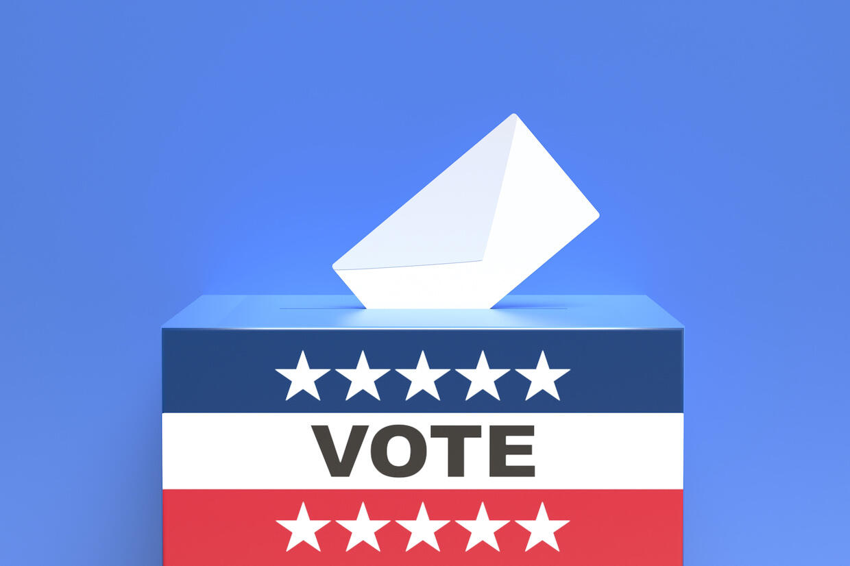 An envelope is placed into a box with "VOTE" on its side.