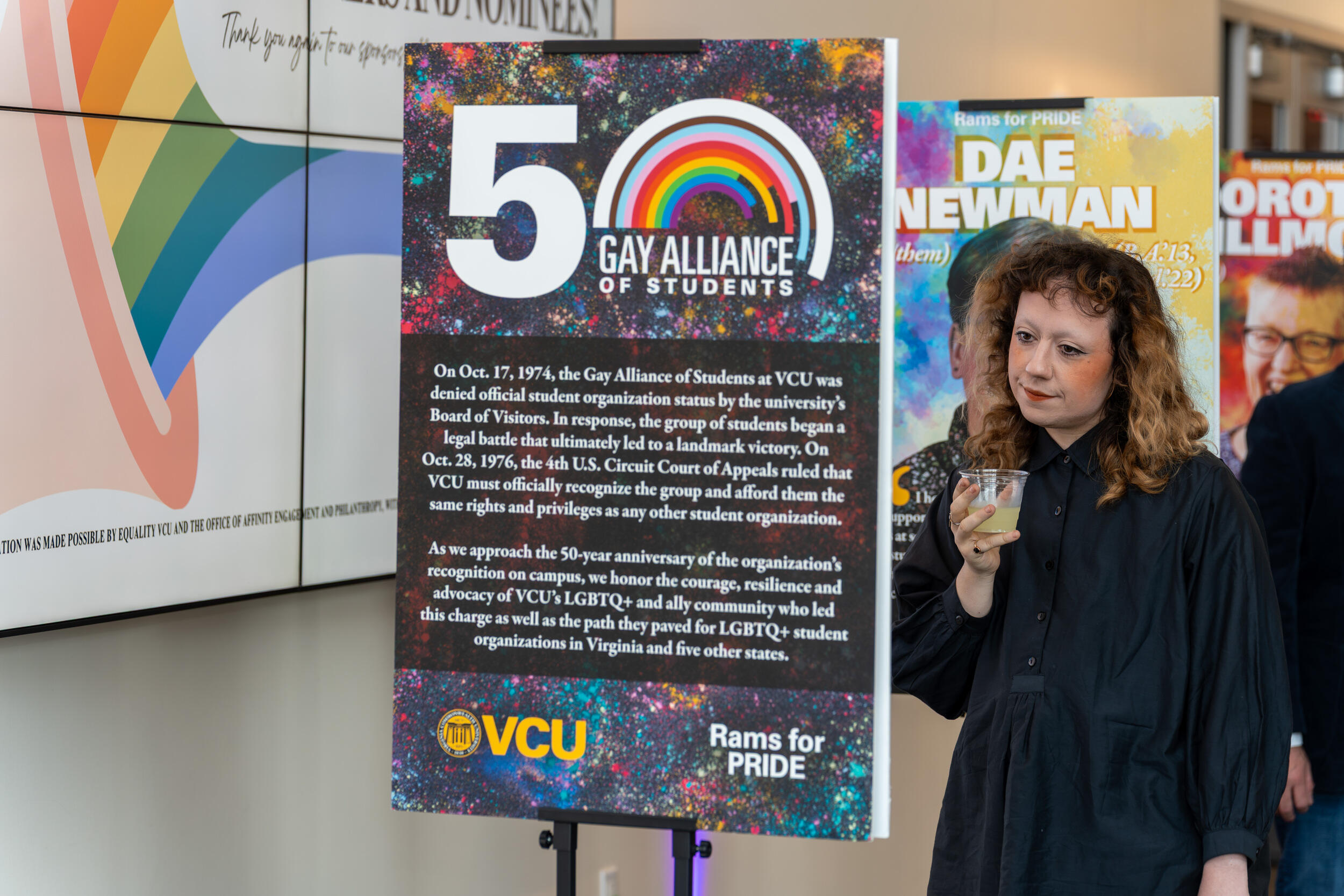 A photo of a person reading a sign about the 50th anniversary of the Gay Alliance of Students. 