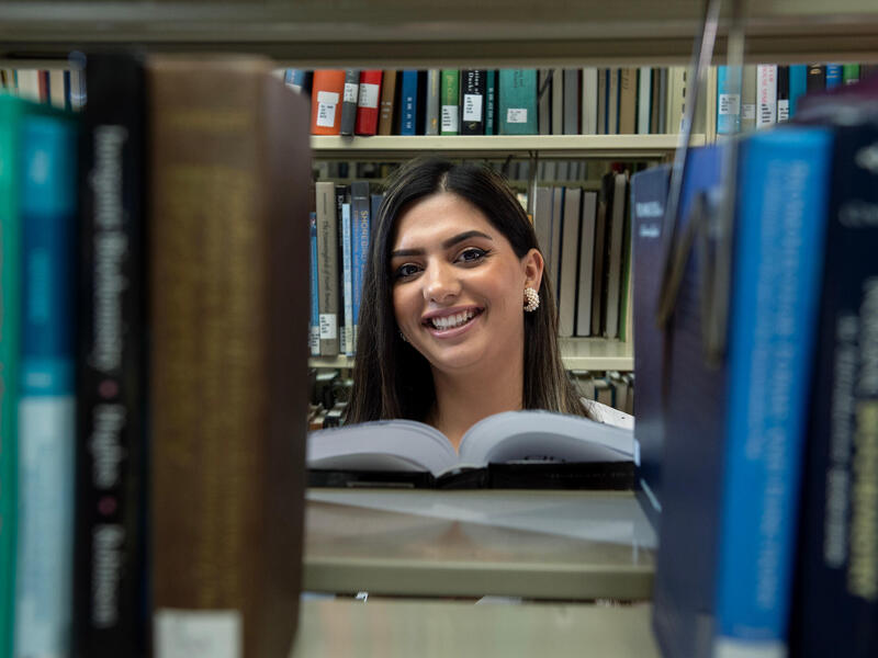 A smiling woman is seen through an opening in a shelf of books.