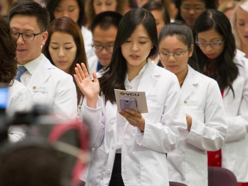 People wearing white lab coats looking down at something and speaking 