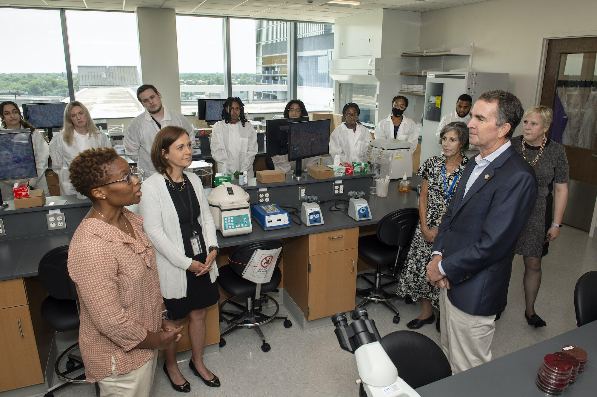 Students look on in the background as (foreground from left) Jenica Harrison, Ph.D., and Melissa Jamerson, Ph.D., professors in the Department of Medical Laboratory Sciences, talk with Teresa Nadder, Ph.D., the department's chair, Virginia Gov. Ralph Northam, M.D., and Susan Parish, Ph.D., dean of the College of Health Professions. 
