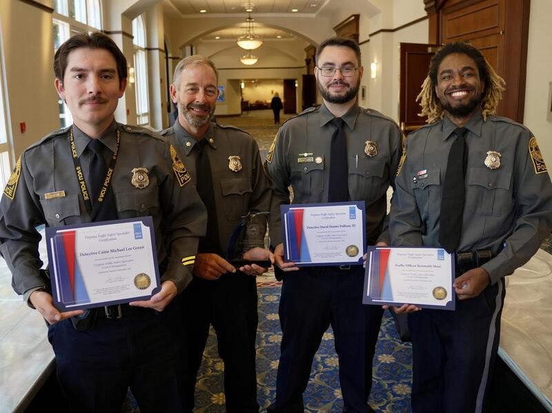 A group photo of four police officers, three are holding certificates.