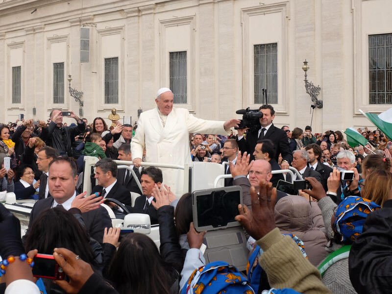 A photo of the pope riding in a car through a crowd of people. 
