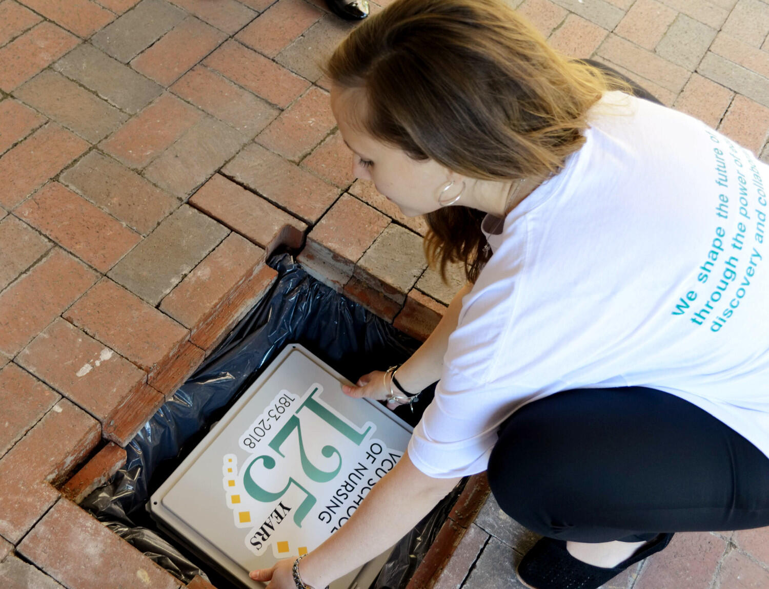 A woman in a white T-shirt puts a box labeled "125" in a hole surrounded by bricks.