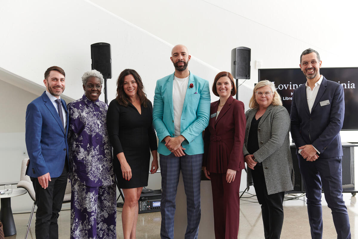 A group photo of seven people standing next to each other in front of speakers 