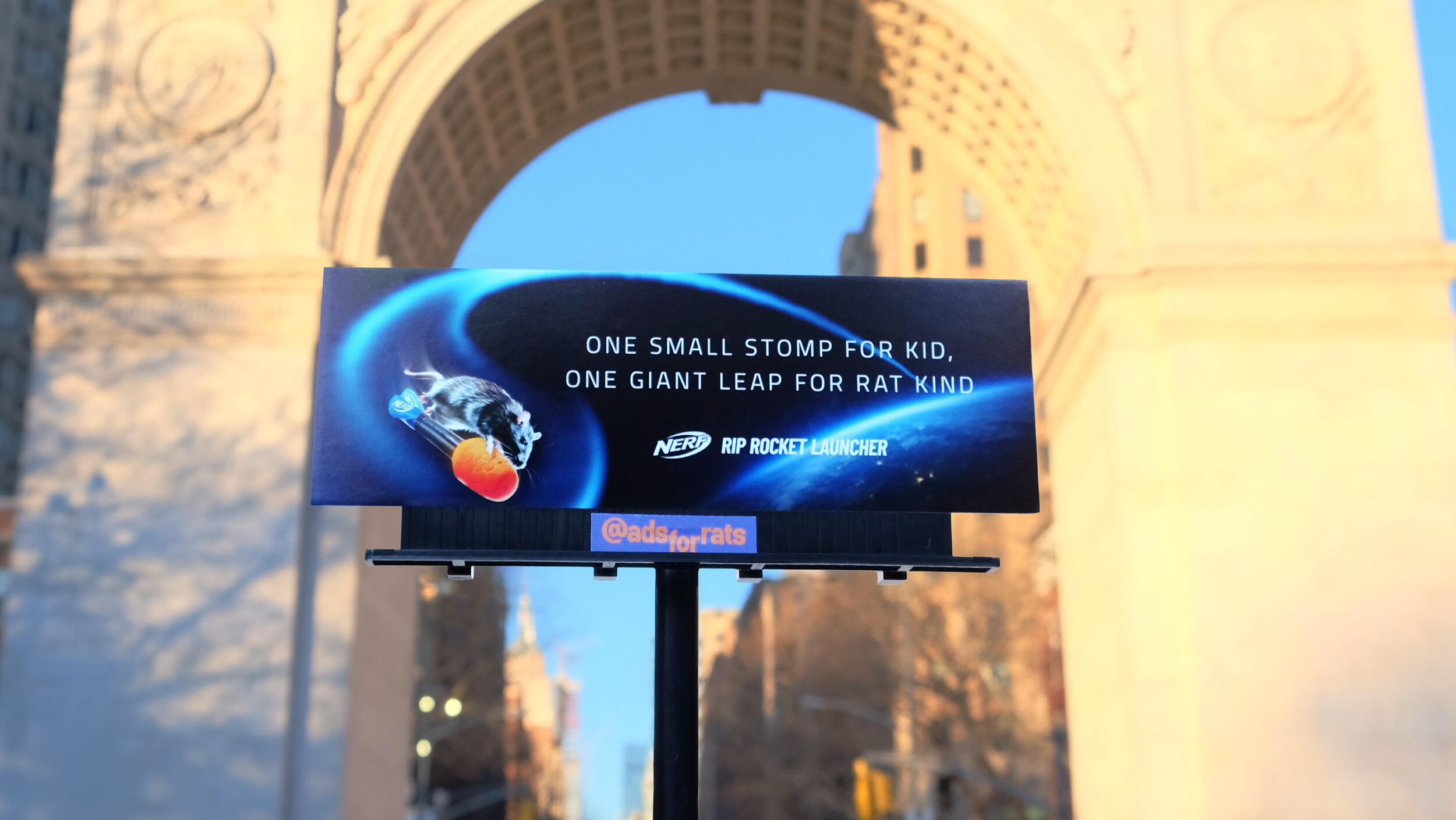 A photo of a bilboard that shows a rat on a nerf bulletthat is flying up from planet earth. White text reads \"ONE SMALL STOMP FOR A KID. ONE GIANT LEAP FOR RAT KIND.\" \"NERF RIP ROCKET LAUNCER.\"