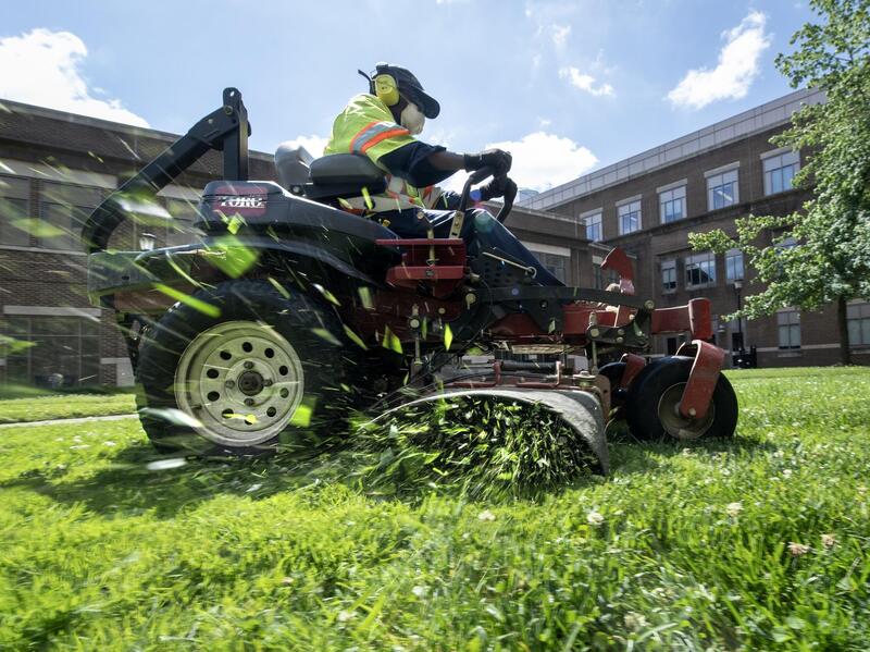 A photo of a man cutting grass on a riding lawnmower. 