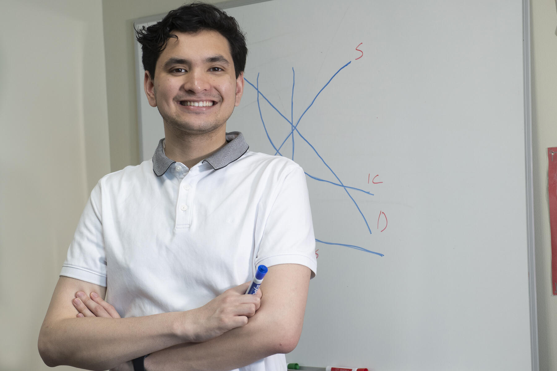 Michael Portillo smiling with his arms crossed holding a marker in front of a white board 