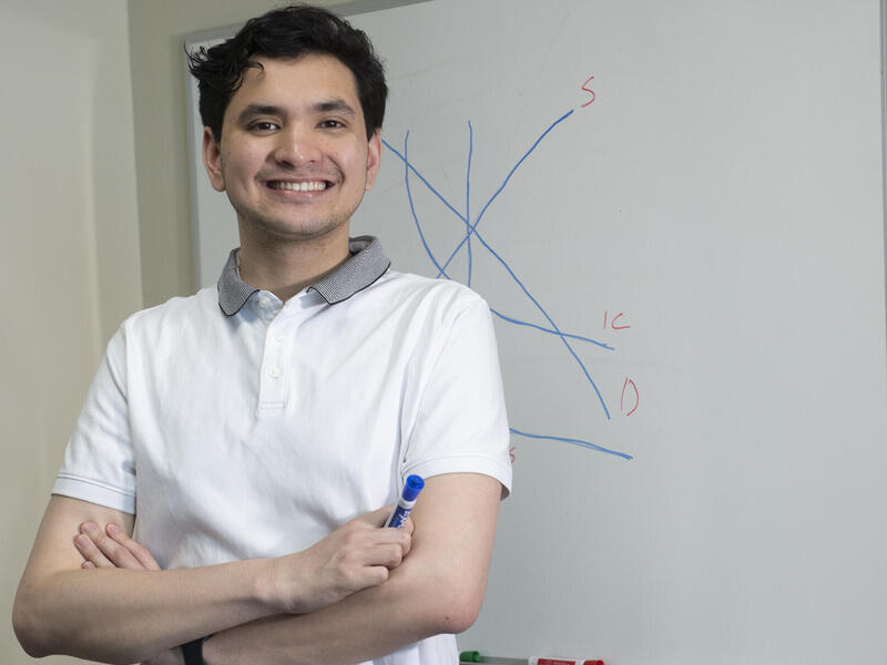 Michael Portillo smiling with his arms crossed holding a marker in front of a white board 