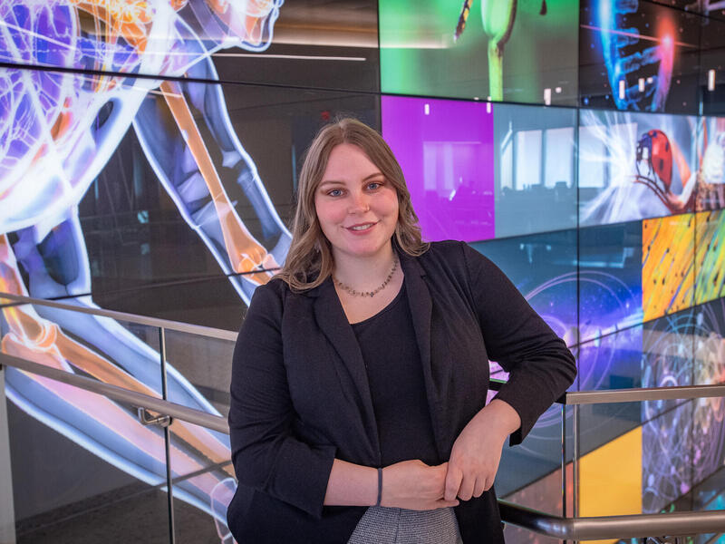 A photo of a woman from the waist up. Her right arm is lenaing on a railing. 