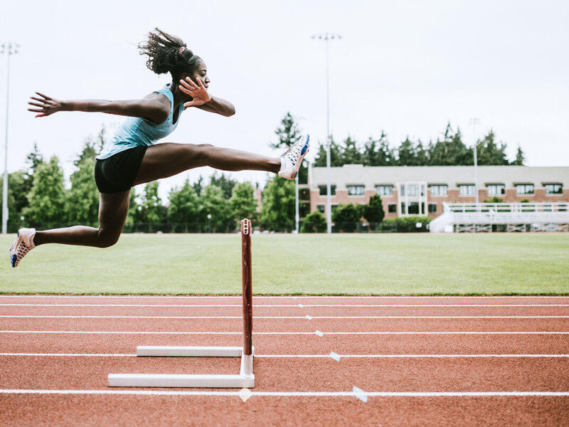 A woman jumping over a hurdle on a track field 