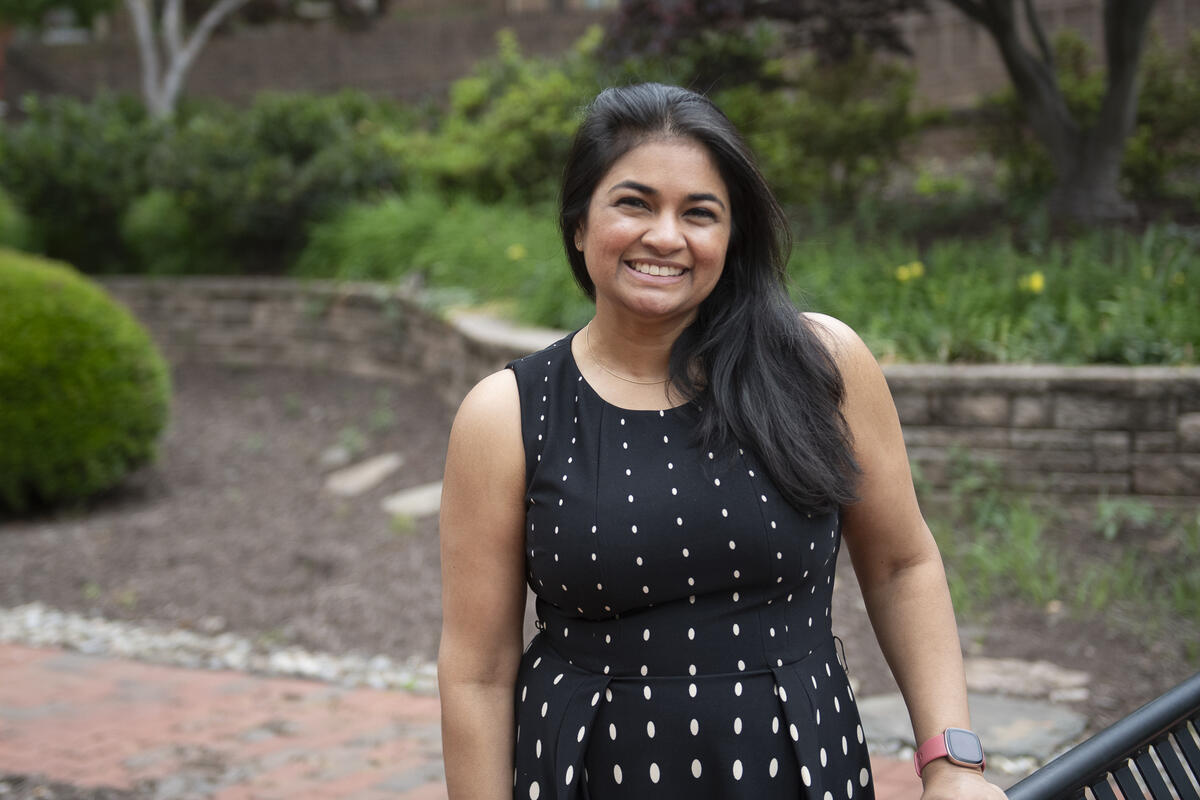 A photo of a woman from the waist up standing outside and smiling. 