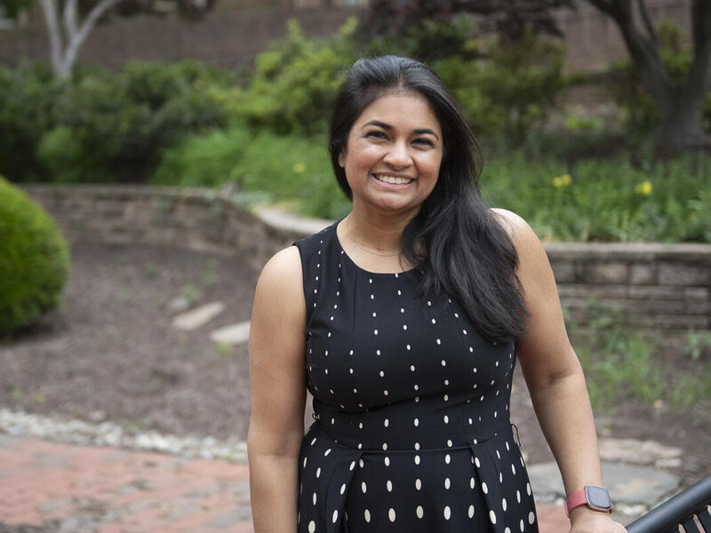 A photo of a woman from the waist up standing outside and smiling. 