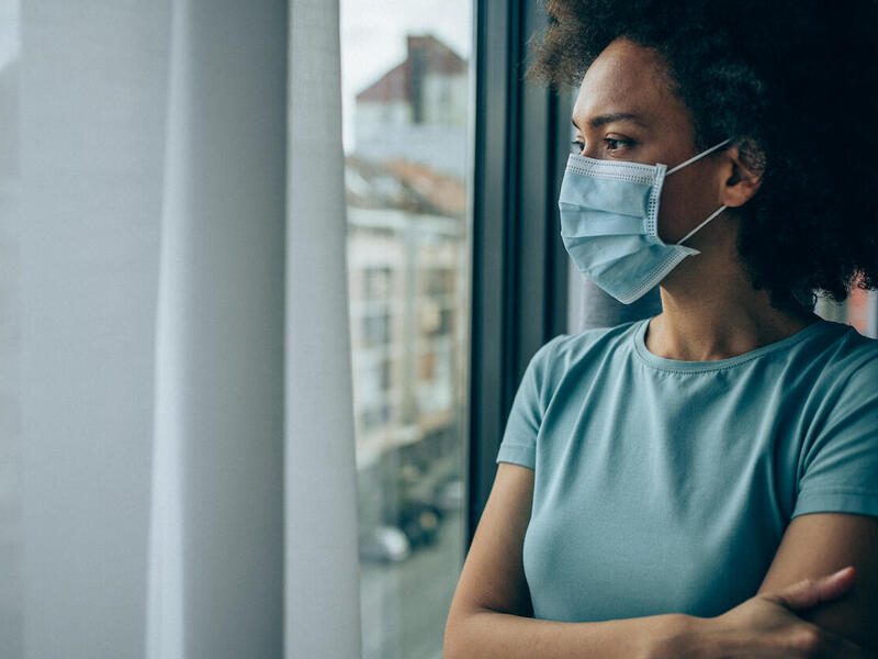 woman wearing a mask and looking out the window
