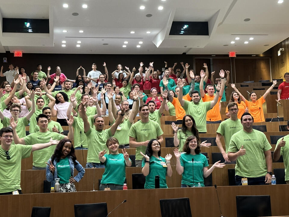 A group of medical students standing with their arms raised up in the air. 