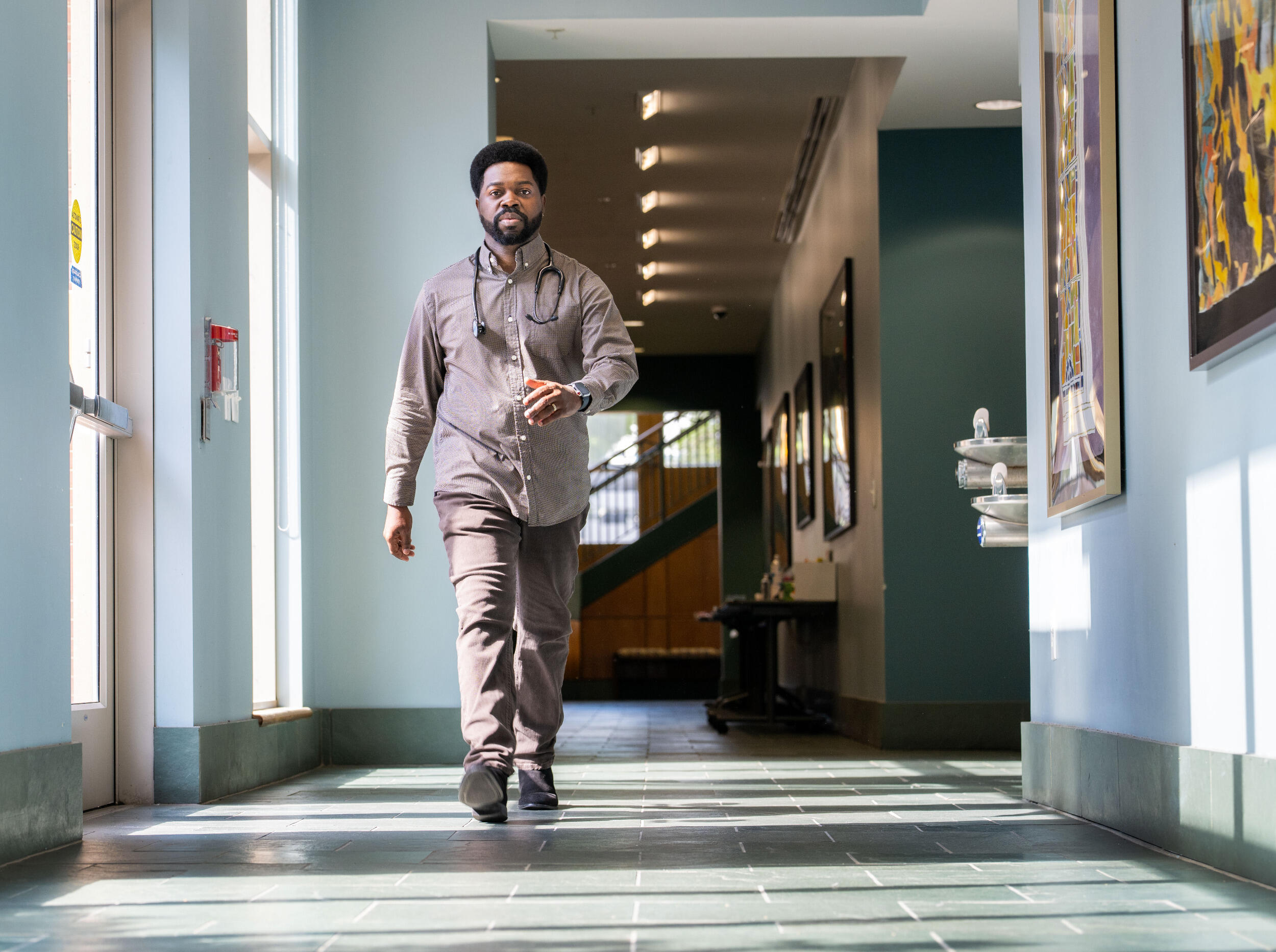 A man with a stethoscope around his neck walks down a hallway.
