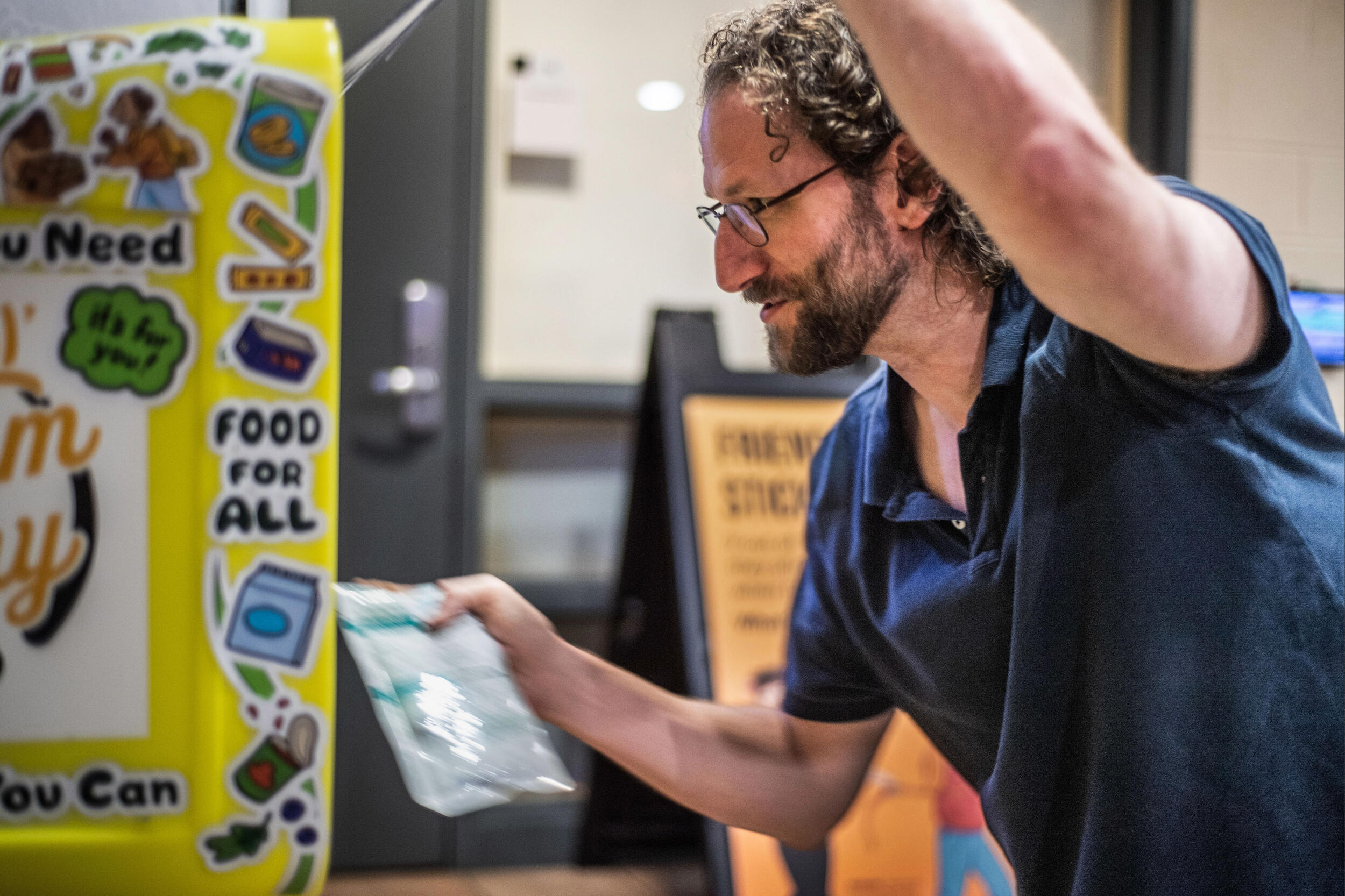 A photo of a man putting a bag into a yellow ram pantry. 