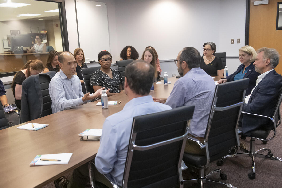A group of people sitting around a long table in a white room. 