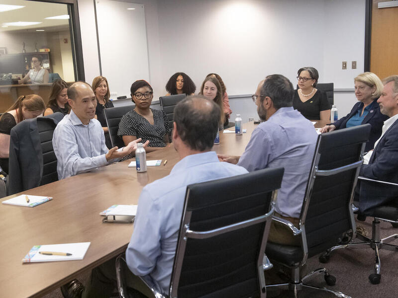 A group of people sitting around a long table in a white room. 