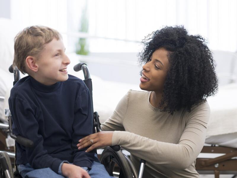 A child in a wheel chair sitting to the left of a woman kneeling down next to him. 