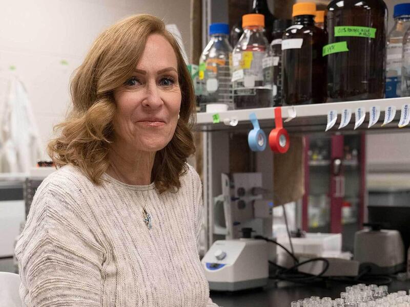 A woman wearing a beige sweater sitting next to a table with testing equipment. 