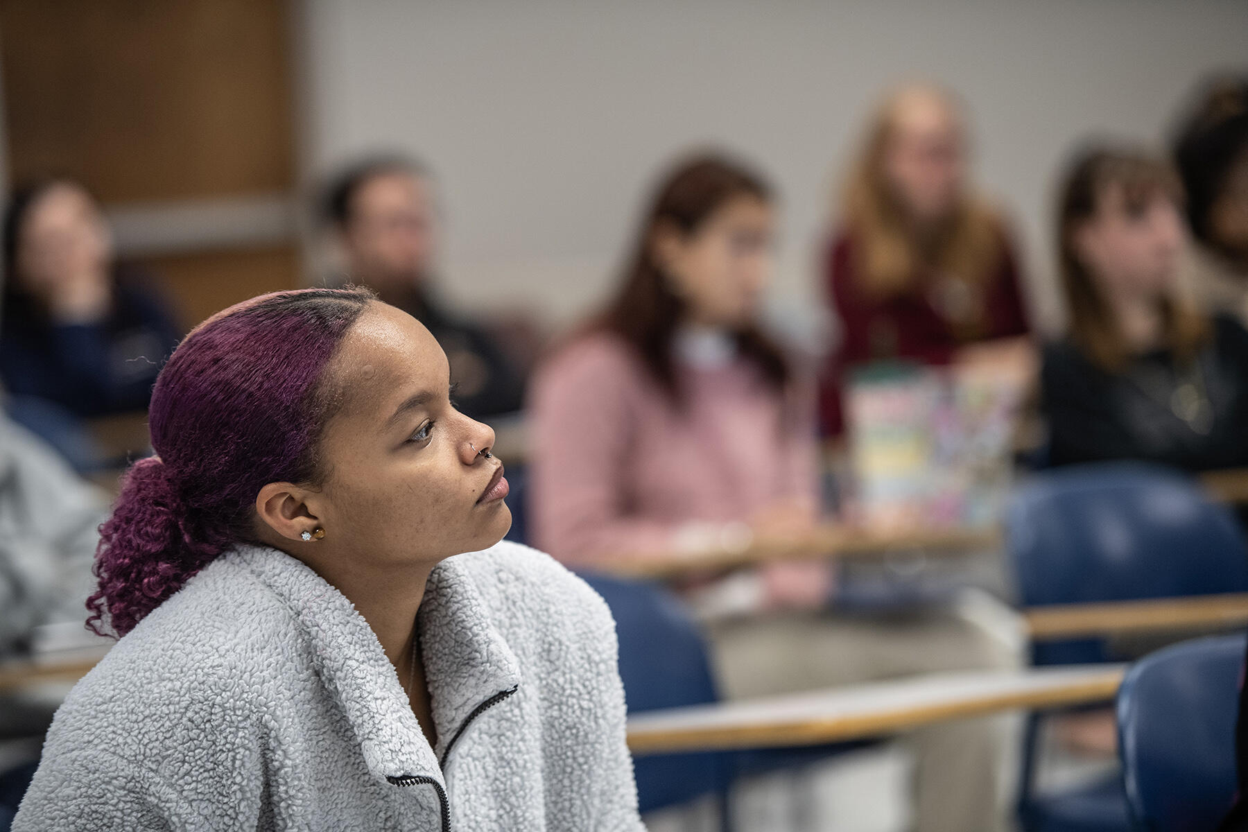 A photo of a woman sitting in a classroom filled with students. 